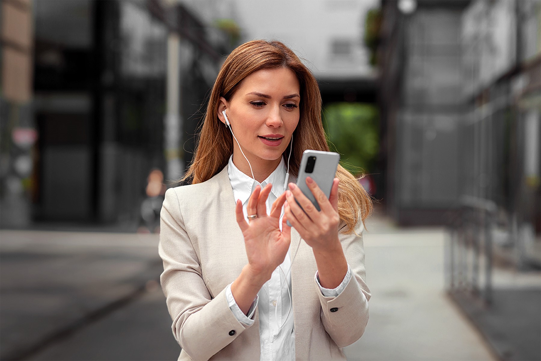 a stock image of a woman outside in a business suit using a smartphone with a headset